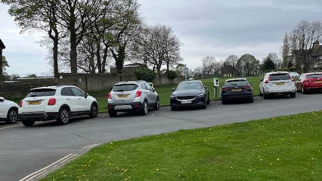 Free parking area with several parked cars, trees in the background, and grassy space in Exley, Yorkshire.