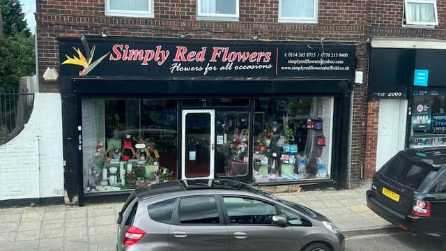 Florist shop front with "Simply Red Flowers" sign, displaying flowers and gifts in the window, parked cars nearby.