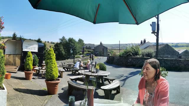 The Lamb Inn features outdoor seating, lush greenery, and a scenic view of the Yorkshire countryside under a large umbrella.