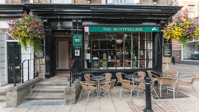 The Montpellier bar features a black facade, large windows, outdoor seating, and vibrant flower baskets.