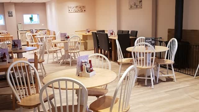 Cozy coffee shop interior with wooden tables, white chairs, and a warm atmosphere, featuring a stove and soft lighting.