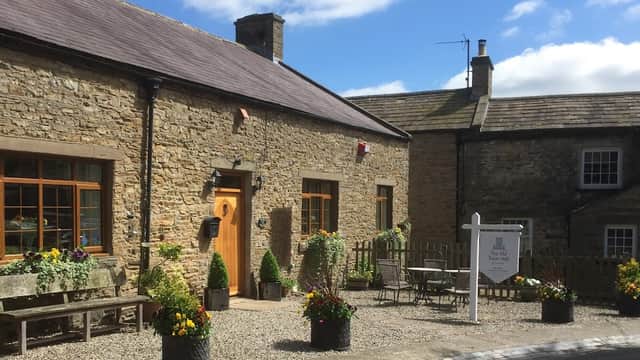 Charming stone building with flower pots, outdoor seating, and a welcoming sign in a picturesque Yorkshire village.