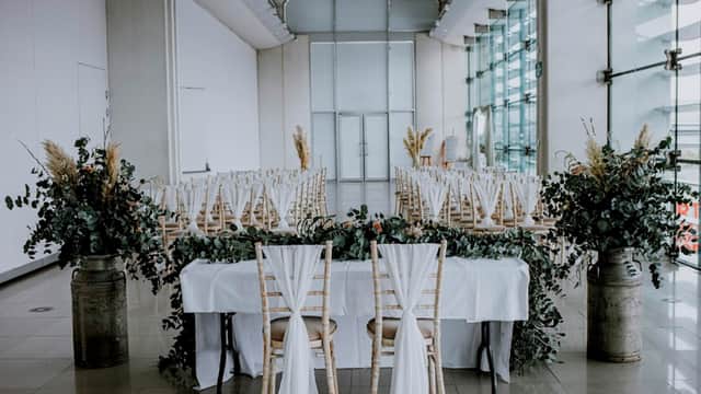 Elegant wedding setup with white drapes, greenery, and rustic chairs arranged in a spacious, modern venue.