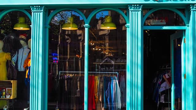 Vintage clothing shop with teal facade, arched windows, colorful garments displayed, and bright green pendant lights.
