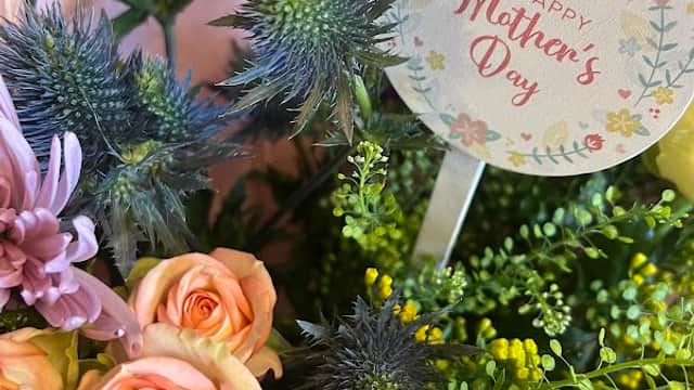 Colorful bouquet featuring roses, thistles, and greenery with a "Happy Mother's Day" tag.