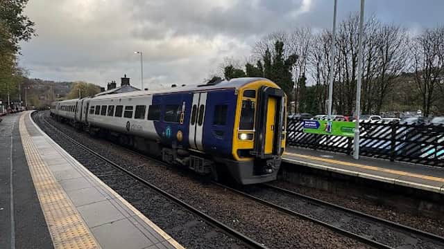 Train approaching the Todmorden station, with tracks and trees lining the background under a cloudy sky.
