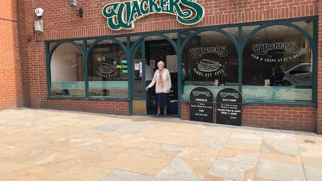 A woman stands at the entrance of a fish and chips shop named "Jackers" in North Cave, Yorkshire, with a brick facade.