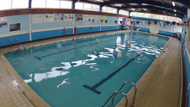 Indoor swimming pool with clear water, colorful beach balls, and safety equipment along the sides. Brightly lit area.
