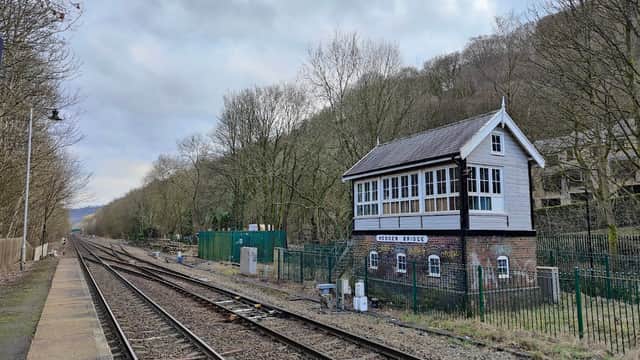 Historic signal box beside railway tracks, surrounded by trees and fencing, with a cloudy sky above.