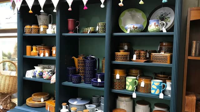 Colorful kitchenware displayed on shelves, including teapots, mugs, and jars, with decorative bunting above.