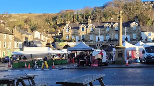 Quaint café with outdoor seating, market stalls, and historic buildings under a clear blue sky in Settle, Yorkshire.