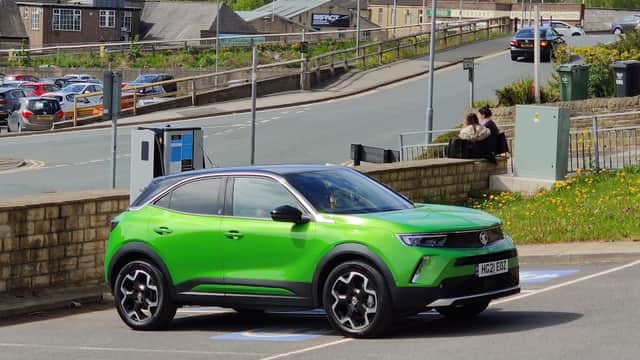 Bright green car parked in a Pay & Display lot, with buildings and trees in the background, and people sitting nearby.