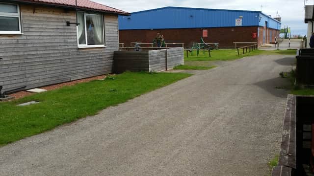 Beachside chalets with a gravel path, grassy areas, and nearby blue commercial building in Wilsthorpe, Yorkshire.