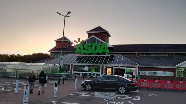 Asda Killingbeck Superstore with a large green sign, shopping trolleys, and two people walking towards the entrance at sunset.