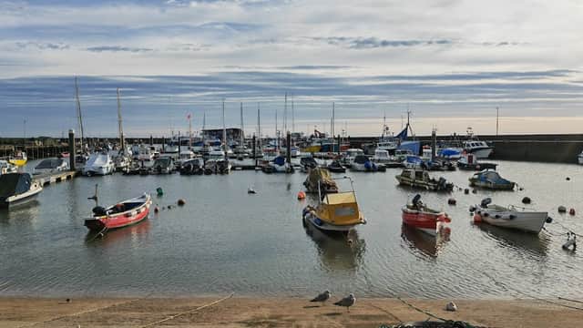 Boats moored in a calm harbor, with a cloudy sky and distant pier visible in Bridlington, Yorkshire.