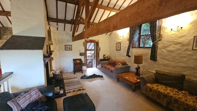 Cozy living area with high wooden beams, comfortable sofas, a coffee table, and natural light from windows.