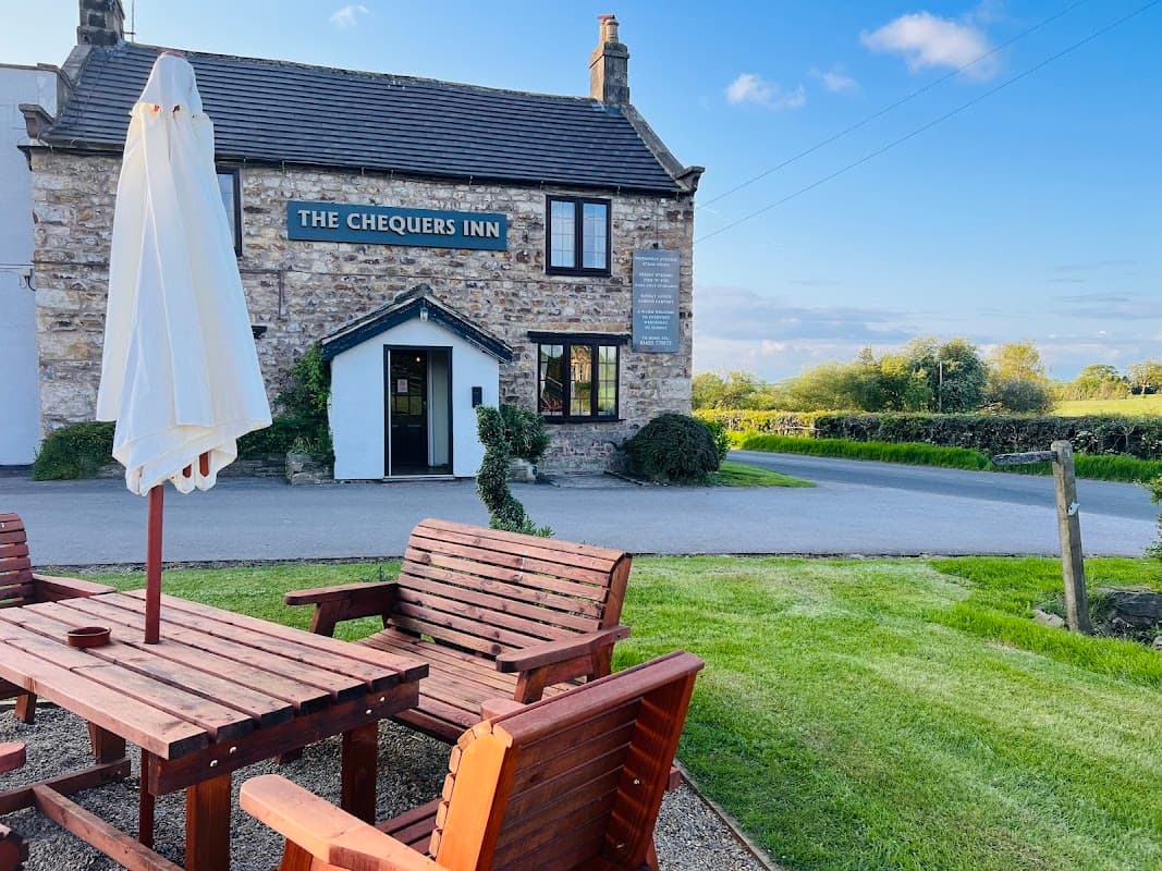 The Chequers Inn features a stone exterior, outdoor seating, and a green landscape in Bishop Thornton, Yorkshire.