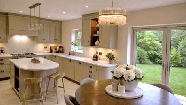 Modern kitchen with light cabinetry, an island, and a round dining table adorned with flowers, overlooking a garden.