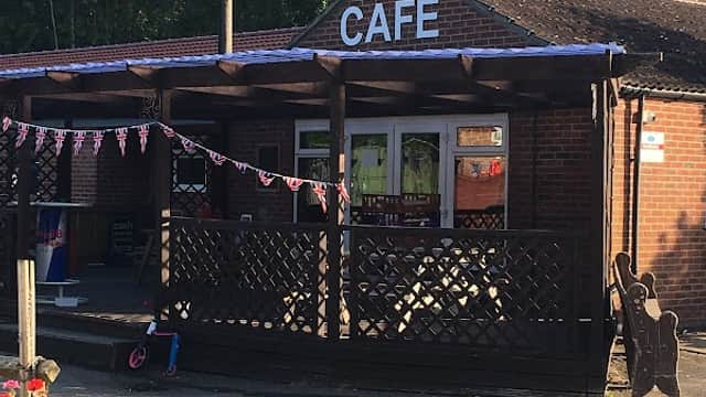 Café building with wooden porch, bunting, and flower pots, set in a sunny outdoor area at Woodland Lakes, Yorkshire.