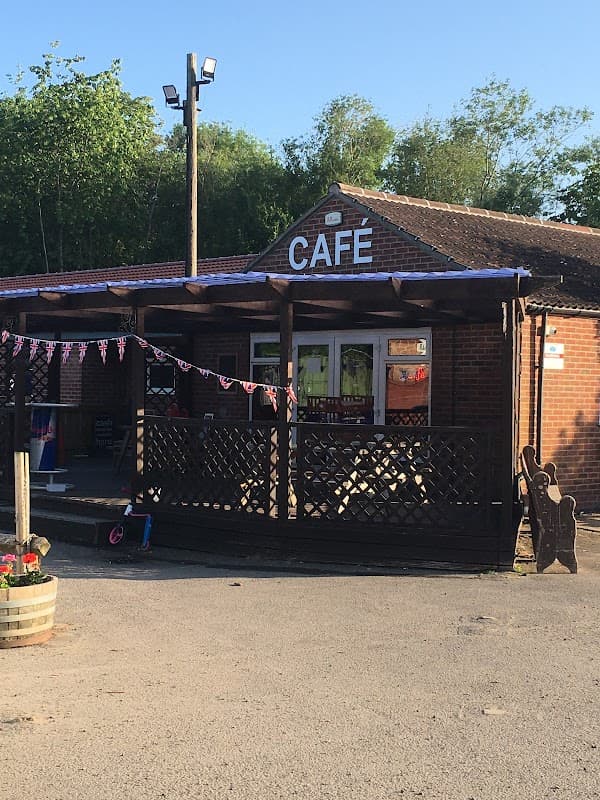 Café building with wooden porch, bunting, and flower pots, set in a sunny outdoor area at Woodland Lakes, Yorkshire.