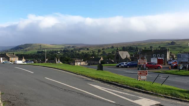 Reeth Public Toilets sign with a scenic view of rolling hills and a village in the background.