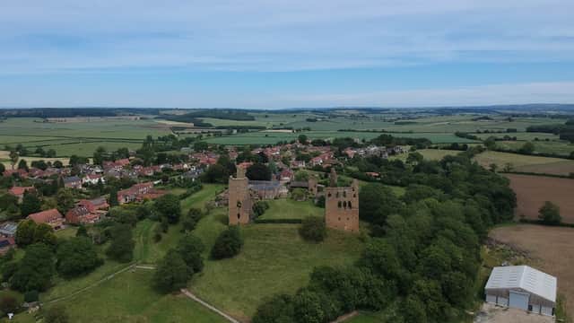 Aerial view of Sheriff Hutton Village Hall surrounded by green fields and historic ruins, with a village in the background.