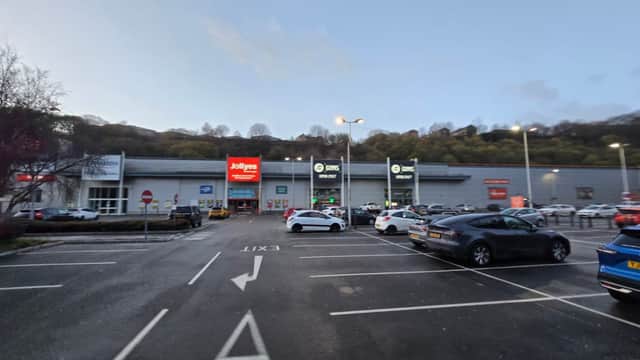 Car park with multiple vehicles, shops in the background, and clear exit signage in Ovenden, Yorkshire.