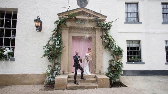 Couple celebrating at The Croft Hotel entrance, adorned with flowers and greenery, with confetti falling around them.