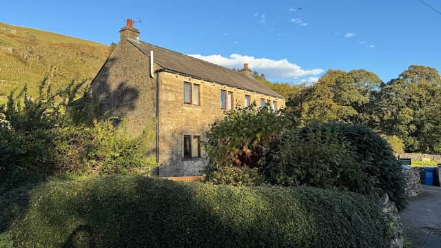 Stone cottage surrounded by greenery, with a clear blue sky and hills in the background, located in Litton, North Yorkshire.