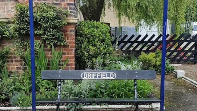 Driffield station sign with a bench, surrounded by greenery and a brick wall.