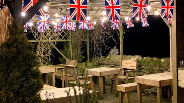 Wooden picnic tables under a canopy adorned with Union Jack flags and string lights at Wuthering Heights Inn campsite.