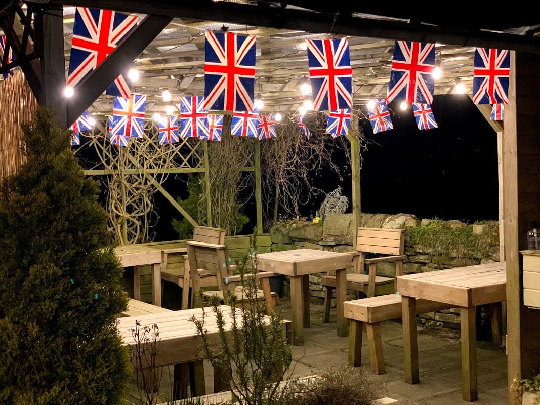 Wooden picnic tables under a canopy adorned with Union Jack flags and string lights at Wuthering Heights Inn campsite.