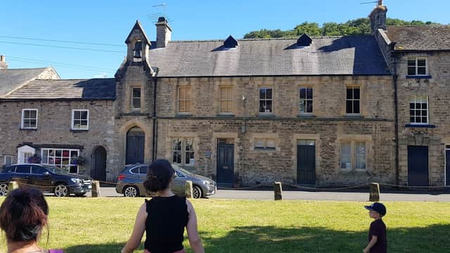 Historic stone buildings with slate roofs, grassy area in front, and people walking nearby in Yorke Square, Richmond.