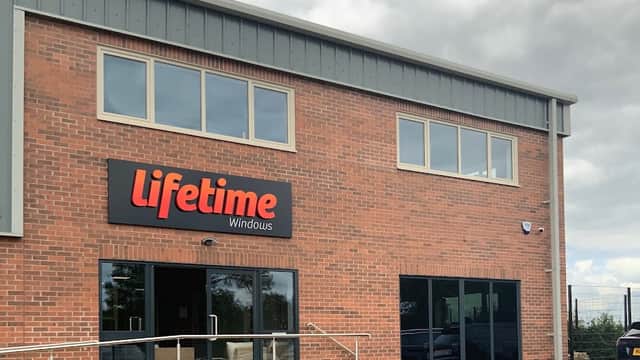 Brick building with large windows, "Lifetime Windows" sign, and a paved area in front. Cloudy sky in the background.