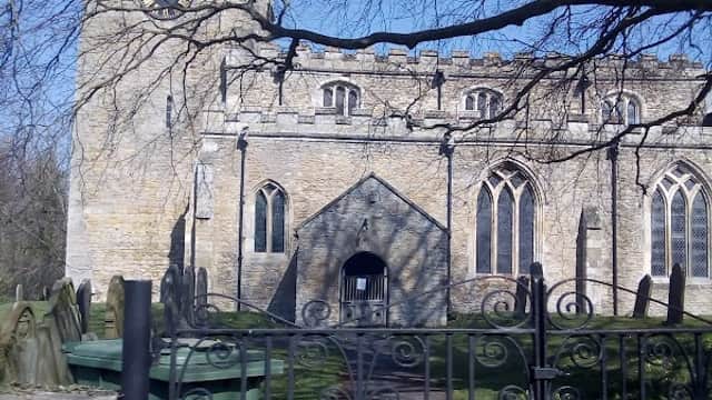 Stone church with a tall clock tower, surrounded by trees and a wrought iron gate, under a clear blue sky.