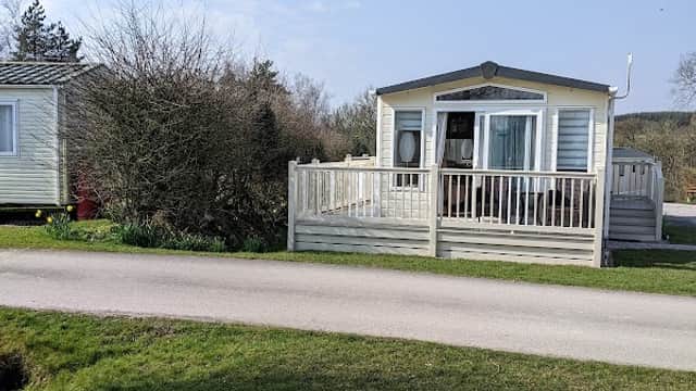 Caravan with a wooden deck surrounded by greenery at Crow Trees Caravan Park, Wrigglesworth, Yorkshire.