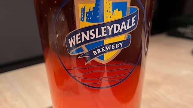 A pint of amber beer in a glass featuring the Wensleydale Brewery logo.