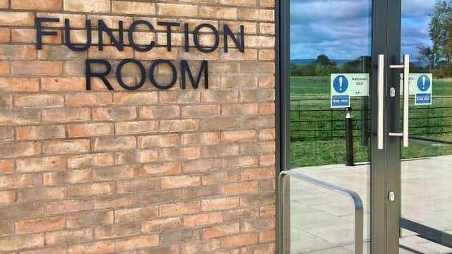 Sign for "Function Room" on a brick wall with glass doors, overlooking green fields in Holme, North Yorkshire.