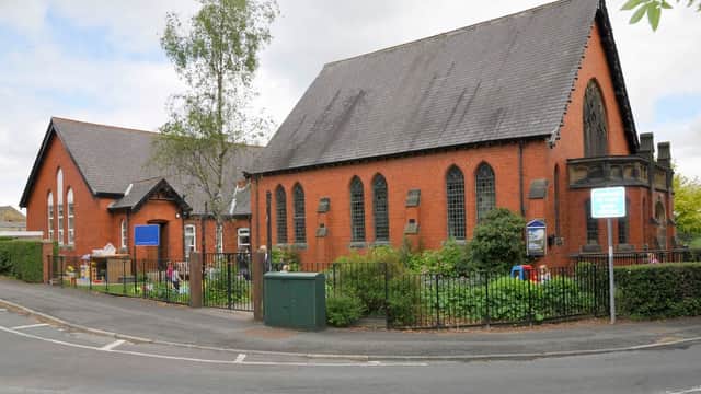 Red brick building with large windows, surrounded by greenery and a fence, located at a street corner in Burn Bridge.