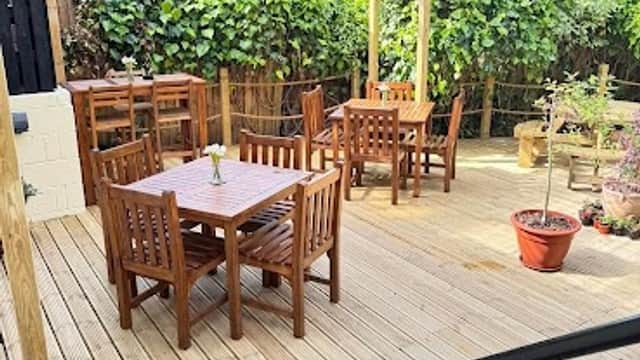 Wooden outdoor seating area with tables and chairs, surrounded by greenery and potted plants at The Butchers Arms.