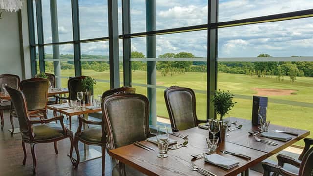 Elegant dining area with wooden tables, plush chairs, and large windows overlooking lush green countryside.
