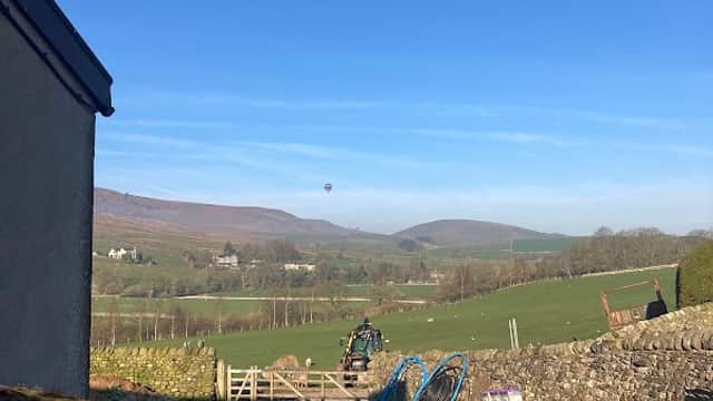 Hartlington Fencing Supplies with a clear blue sky, rolling green hills, and a distant hot air balloon.