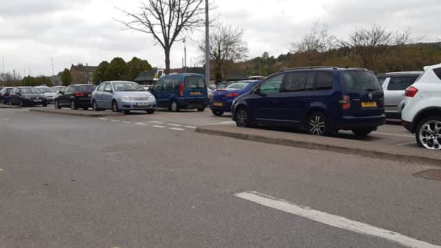 Busy car park with various parked vehicles, trees in the background, and cloudy skies overhead.