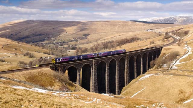 A scenic view of a viaduct with a train crossing, surrounded by rolling hills and fields under a blue sky.