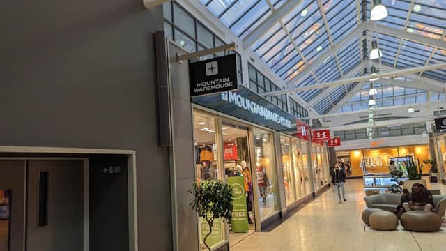Mountain Warehouse storefront with large windows, clothing displays, and shoppers in a mall setting.