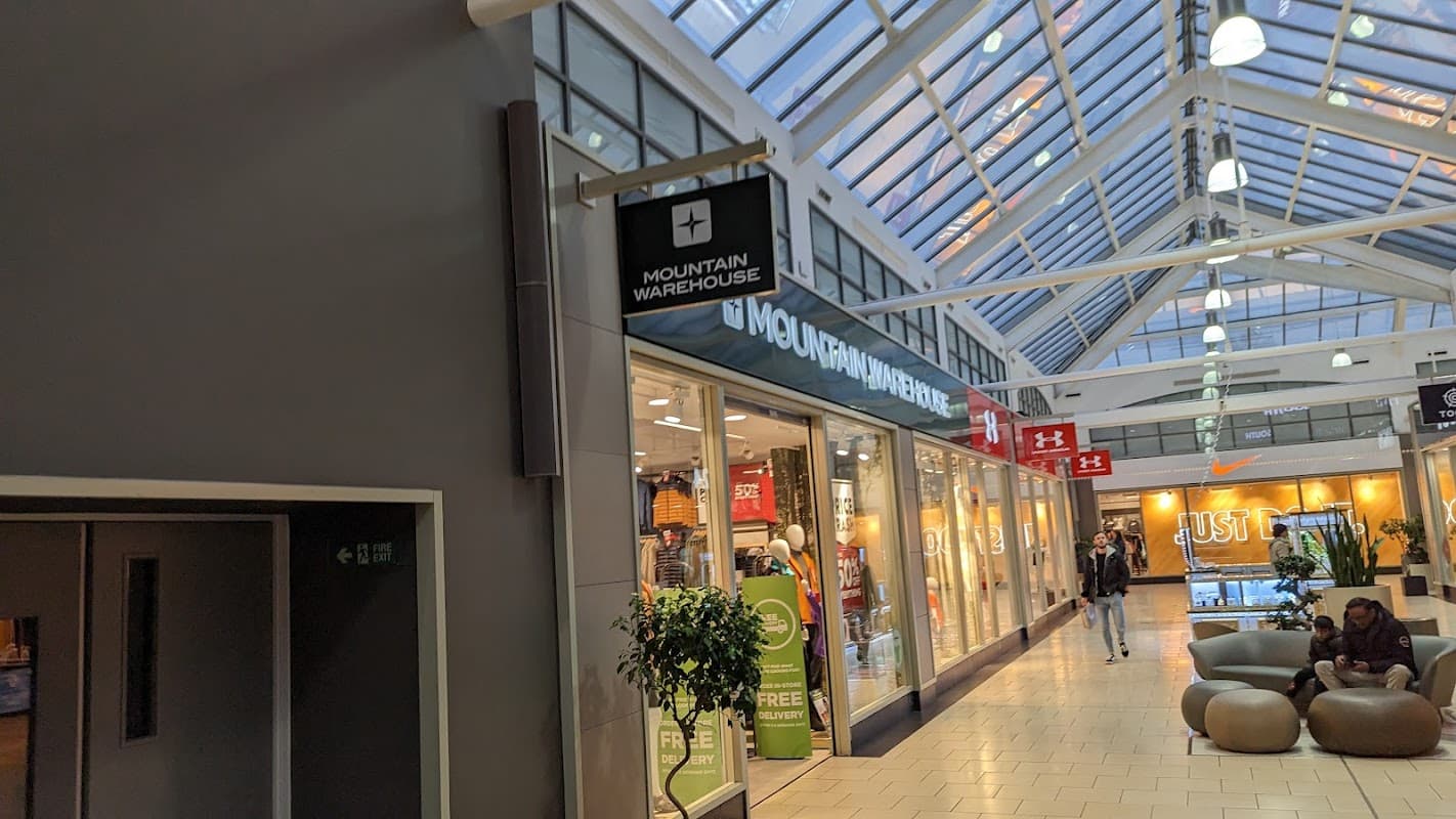 Mountain Warehouse storefront with large windows, clothing displays, and shoppers in a mall setting.