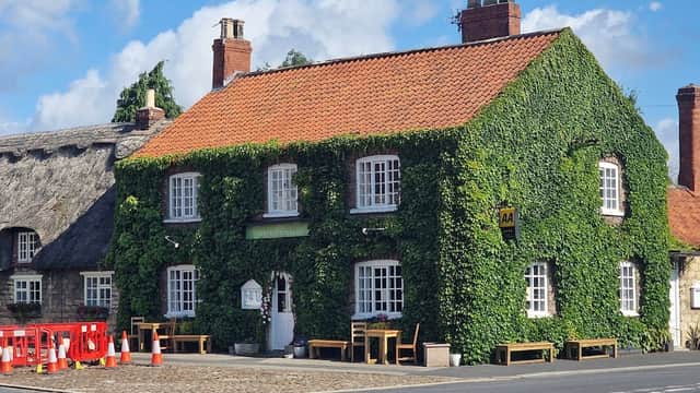 The Wentworth Arms hotel, covered in ivy, features a red-tiled roof and wooden benches outside on a sunny day.