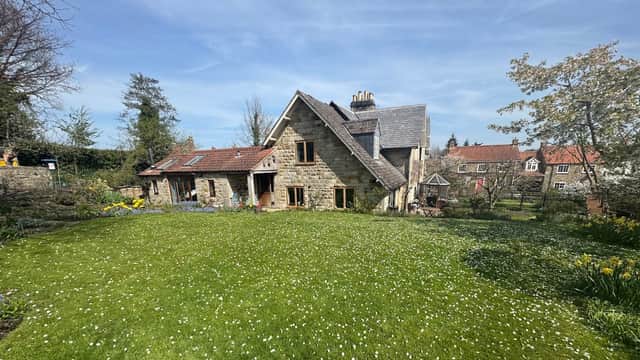Charming stone hotel with a lush green lawn, colorful flowers, and trees under a clear blue sky in Yorkshire.