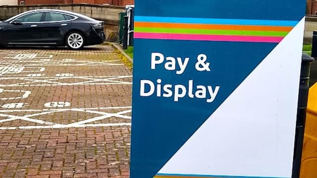 Millgate Car Park sign with "Pay & Display" instructions, featuring a car and nearby residential buildings in Thirsk.
