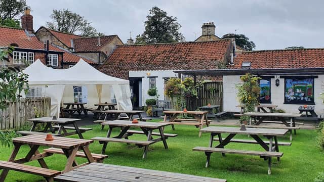 Outdoor seating area with wooden picnic tables, a white marquee, and a charming pub building in Old Malton, Yorkshire.
